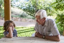 Grandfather and grandson sitting on wooden table and talking outdoors. — Stock Photo