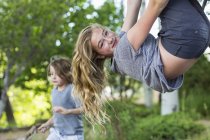 Blonde teenage girl hanging upside down from tree in garden. — Stock Photo