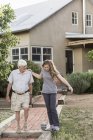 Teenage girl and grandfather walking along path by house. — Stock Photo