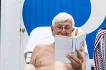 Hombre mayor en el libro de lectura junto a la piscina - foto de stock