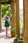 Teenager-Mädchen gießt Pflanzen auf Holzterrasse. — Stockfoto