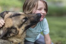 Petit garçon embrassé par un chien berger allemand à l'extérieur . — Photo de stock