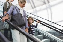 Усміхнений маленький хлопчик подорожує на ескалаторі аеропорту з мамою і сестрою . — стокове фото