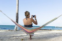 Женщина отдыхает в гамаке, фотографируется со смартфоном, на острове Кайман — стоковое фото