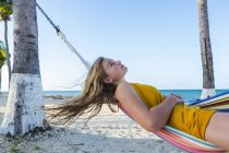 Blondes Teenager-Mädchen ruht sich in bunter Hängematte am Strand aus. — Stockfoto