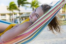 Blonde teenage girl resting in colorful hammock on beach. — Stock Photo