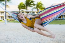 Блондинка-подросток отдыхает в разноцветном гамаке на пляже . — стоковое фото