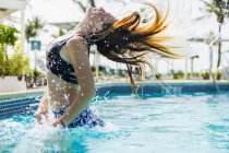 Blonde teenage girl leaping out of pool and tossing wet hair. — Stock Photo
