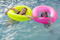 Frères et sœurs jouant dans la piscine avec des flotteurs colorés . — Photo de stock