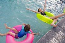 Siblings playing in pool in colorful float. — Stock Photo