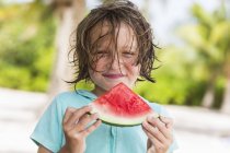Lächelnder Junge isst Wassermelonenscheibe im Freien am Strand. — Stockfoto