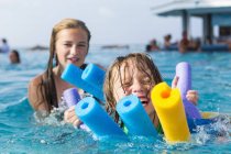 Siblings playing in pool in colorful floats. — Stock Photo