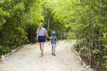 Rear view of teen sister and little brother walking on nature path. — Stock Photo