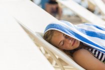 Blonde teenage girl reclining in beach chair with towel on head. — Stock Photo