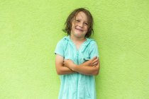 Sorrindo menino pré-escolar posando com os braços cruzados na frente da parede verde . — Fotografia de Stock