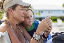 Mère et enfant d'âge préscolaire regardant smartphone à la plage . — Photo de stock