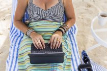Взрослая женщина с ноутбуком на пляже, остров Гранд Кайман — стоковое фото