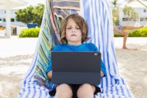 Дошкольный мальчик с ноутбуком в шезлонге на пляже
. — стоковое фото