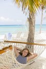 Teenage girl relaxing in hammock on tropical beach. — Stock Photo