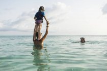 Preschooler figlio da madre spalle saltando in oceano al tramonto . — Foto stock