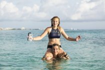 Donna adulta in piedi in acqua oceanica al tramonto con figlia sulle spalle — Foto stock
