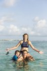 Donna adulta in piedi nell'acqua dell'oceano al tramonto con i bambini — Foto stock