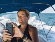 Взрослая женщина фотографируется со смартфоном на лодке — стоковое фото