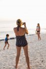 Мати фотографує дітей, які насолоджуються пляжем на заході сонця на острові Ґранд Кайман. — стокове фото
