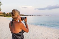 Взрослая женщина фотографируется со смартфоном на пляже — стоковое фото