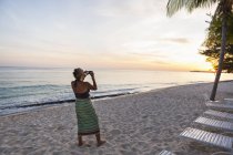 Femme adulte prenant des photos avec smartphone sur la plage — Photo de stock