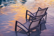 Liegestühle im Poolwasser bei Sonnenuntergang. — Stockfoto