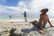 Kleiner Junge, der im Wasser läuft, als Mutter zusieht, Grand Cayman Island. — Stockfoto
