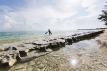 Petit garçon marchant dans l'eau depuis la formation rocheuse avec des nageoires, île Grand Cayman . — Photo de stock
