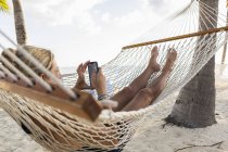 Relaxing mature woman in hammock using smartphone. — Stock Photo