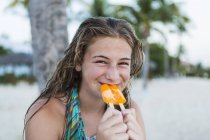 Lächelnde blonde Teenie-Mädchen essen süßes Eis am Stiel am Strand. — Stockfoto