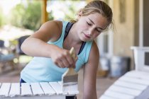 Блондинка дівчина-підліток малює меблі на відкритому повітрі в білій фарбі . — стокове фото