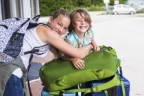Rubia hermana adolescente y hermano pequeño apoyado en el equipaje de viaje . - foto de stock
