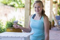 Blonde teen girl painting outdoor furniture in white paint. — Stock Photo