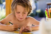 Маленький мальчик без рубашки рисует цветными карандашами на улице . — стоковое фото