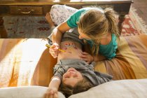 Blonde teen sister drawing with paint onto elementary age brother stomach. — Stock Photo