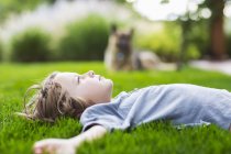 Хлопчик початкового віку лежить на пишному зеленому газоні, дивлячись вгору — стокове фото