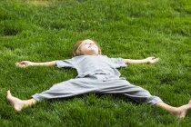 Хлопчик початкового віку лежить на пишному зеленому газоні, дивлячись вгору — стокове фото