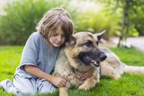 Elementary age boy playing with German Shepherd dog on green lawn — Stock Photo