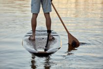 Pernas de homem em pé sobre paddleboard no rio ao amanhecer, visão traseira — Fotografia de Stock