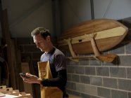 Paddleboard maker con dispositivo mobile in officina — Foto stock