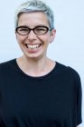 Woman with short grey hair wearing glasses smiling in camera. — Stock Photo