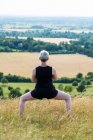 Rear view of woman practicing outdoor yoga on hillside. — Stock Photo