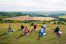 Grupo de mujeres y hombres que participan en clases de yoga al aire libre en una colina . - foto de stock