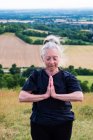 Femme âgée prenant part à un cours de yoga en plein air sur une colline . — Photo de stock