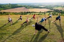 Group of women and men taking part in outdoor yoga class on a hillside. — Stock Photo